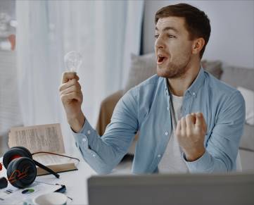 Man sitting in front a computer screen holding a lightbulb